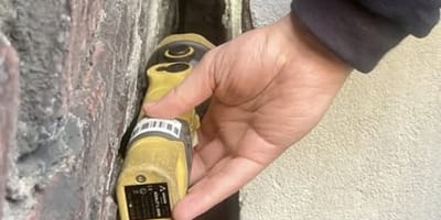 Mann leuchtet mit Taschenlampe in einen Mauerspalt