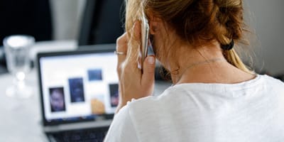 Telefonierende Frau siotzt vor dem Laptop