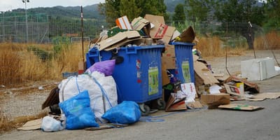 Contenedores de basura llenos con una bolsa al lado