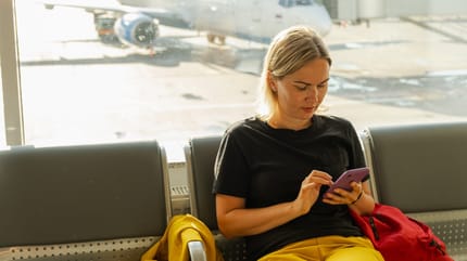 Frau am Flughafen schaut auf ihr Telefon