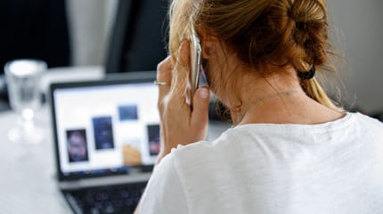Telefonierende Frau siotzt vor dem Laptop