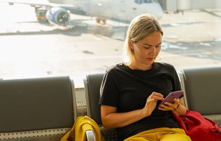 Frau am Flughafen schaut auf ihr Telefon