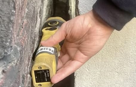 Mann leuchtet mit Taschenlampe in einen Mauerspalt