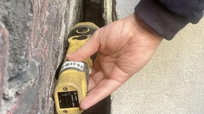 Mann leuchtet mit Taschenlampe in einen Mauerspalt